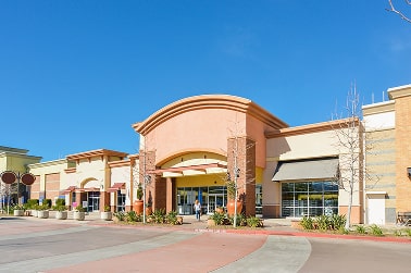 Modern shopping center with a light orange and beige facade under a clear blue sky.